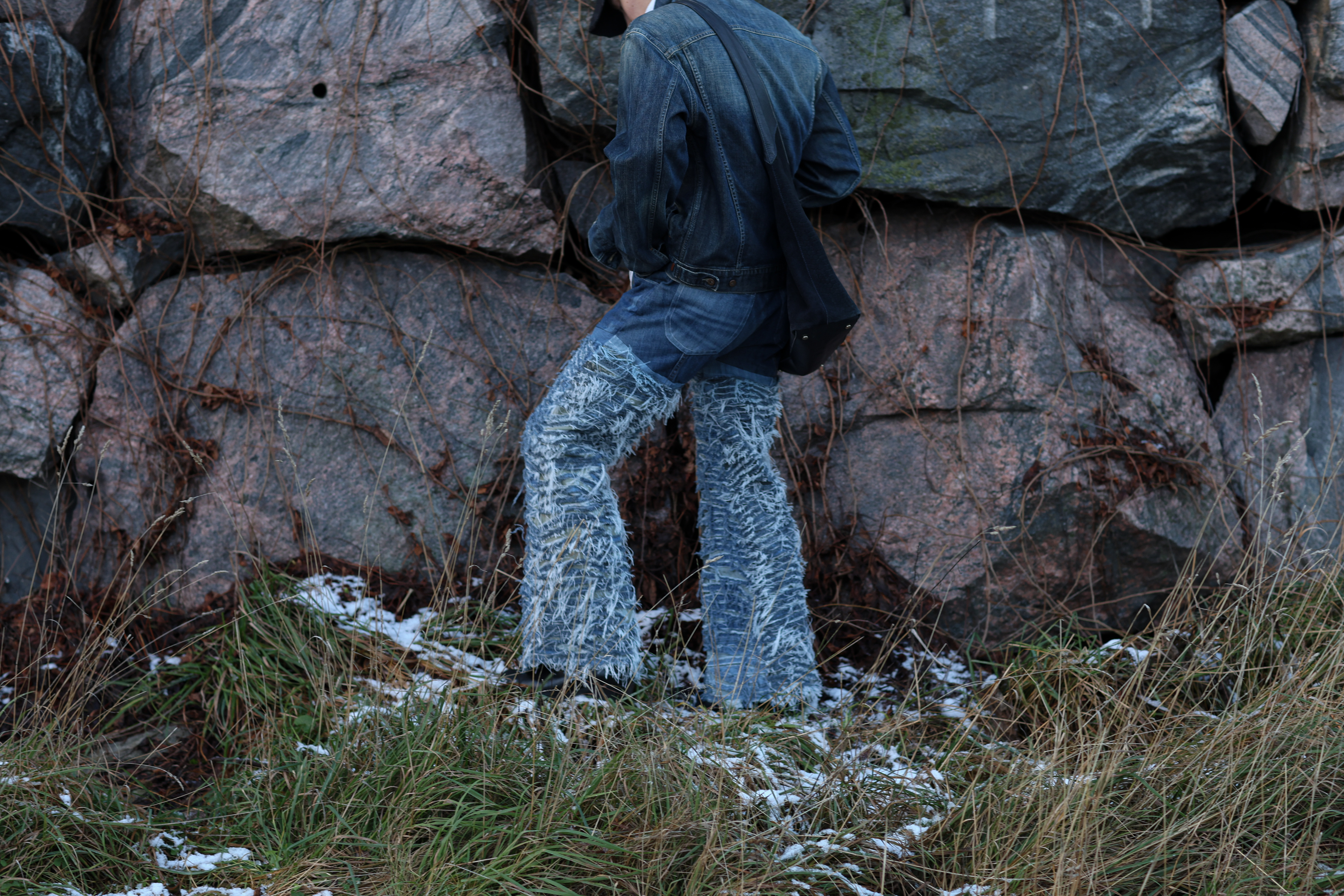Model wearing distressed Lorimer denim beside a rock wall